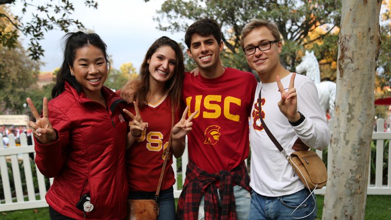 four college students wearing USC shirts smiling and giving the peace sign